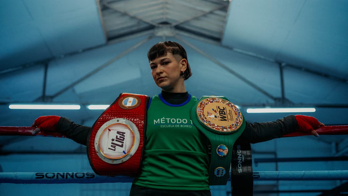 Female boxer in Buenos Aires gym displaying championship belts, showcasing strength and determination.